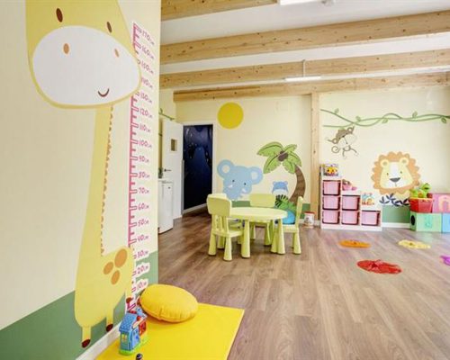 Savia proyectos miniclub infantil interior con mesas y sillas pequeñas y en la pared jirafa elefante león y palmera con cajas en el suelo